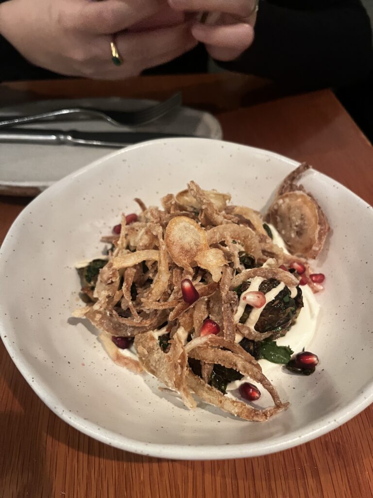 brussels sprouts served with pomegranate and a white sauce, topped with fried onions