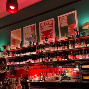 interior of city oltra wine bar with neo-retro style posters, heaps of wine bottles and moody red lighting